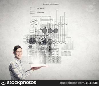 Guy studying finances. Young smiling man with opened book in hands and infographs on wall