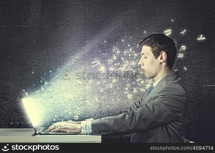 Guy using laptop. Thoughtful young man in suit seriously looking in laptop