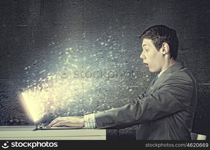 Guy using laptop. Young man in suit looking astonished in laptop. Surfing the internet