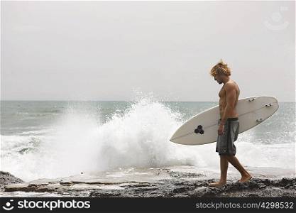 Guy walking on cliff with surfboard ocean behind him