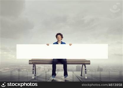 Guy with blank banner. Young man sitting on bench with white banner