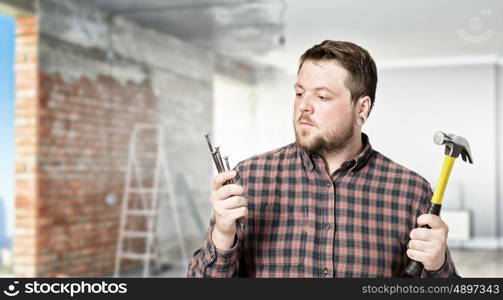 Guy with construction tools. Casual man in checked shirt indoors with hammer and nails