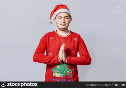 Guy with hands together praying in christmas isolated, concept of person with christmas hat praying and making a wish. Man with christmas hat with praying hands isolated