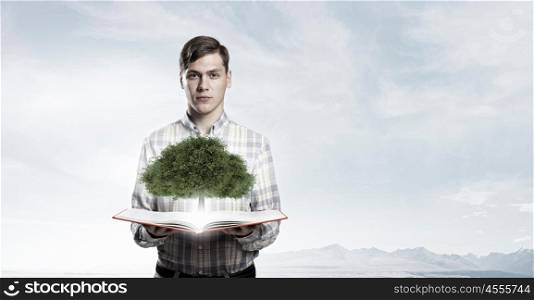 Guy with opened book . Young man with book in hands and green tree on pages