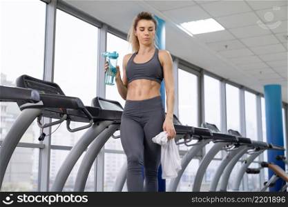 Gym woman working out drinking water standing by fitness machines inside in fitness center. Gym woman working out drinking water standing by fitness machines