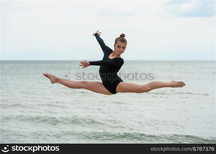 Gymnast Dancer Jumping On The Sea Beach. Young beautiful girl jumps outdoors over sea background