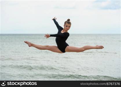 Gymnast Dancer Jumping On The Sea Beach. Young beautiful girl jumps outdoors over sea background