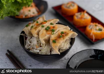 Gyoza in a black cup with a cup of sauce.