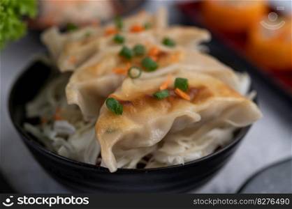 Gyoza in a black cup with Sushi. Se≤ctive focus.