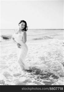 Gypsy young brunette girl in white maxi long dress standing on the waves in sea or ocean. Windy beach. Bohemian lifestyle. Portrait of happy sexy woman.. Gypsy young brunette girl in white maxi long dress standing on the waves in sea or ocean. Windy beach. Bohemian lifestyle. Black and white portrait of happy sexy woman.