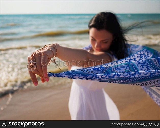 Gypsy young brunette Girl wearing white maxi long dress standing on the sea or ocean beach with mandala silk scarf in hands. Bohemian clothing style. Boho lifestyle. High quality photo. Gypsy young brunette Girl wearing white maxi long dress standing on the sea or ocean beach with mandala silk scarf in hands. Bohemian clothing style. Boho lifestyle