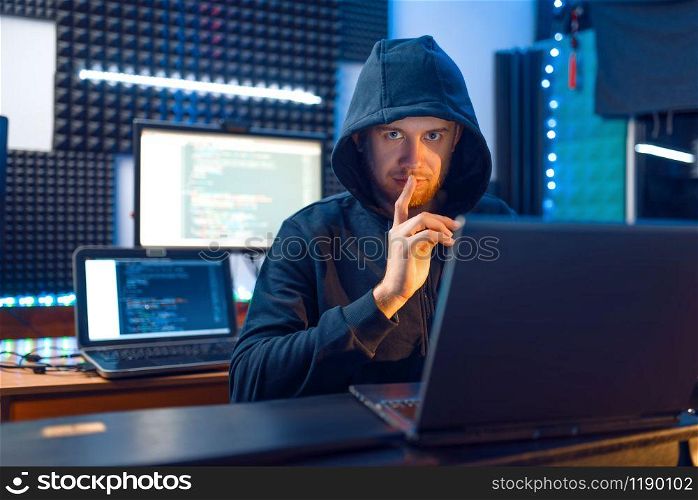 Hacker in hood shows thumbs up at his workplace with laptop and PC, password or account hacking. Internet spy, crime lifestyle. Hacker in hood shows thumbs up, network criminal