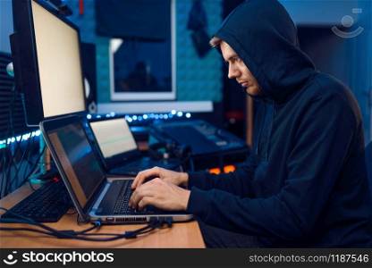 Hacker in the hood sitting at laptop, information hacking. Internet spy, male programmer trying to hack an encrypted network. Hacker sitting at laptop, information hacking