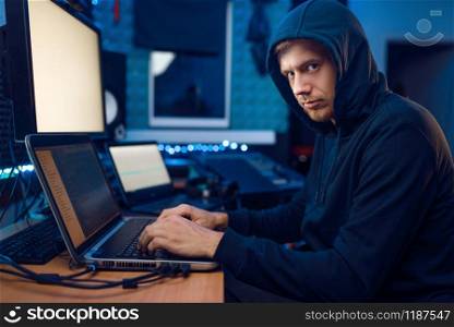 Hacker in the hood sitting at laptop, information hacking. Internet spy, male programmer trying to hack an encrypted network