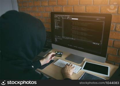 Hacker in the hood working with computer and holding credit card with payment hacking concept.