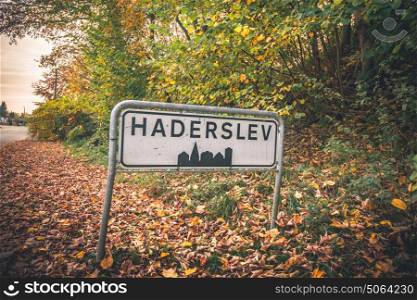 Haderslev city sign by a road in Denmark in the fall with colorful trees and leaves on the groubd