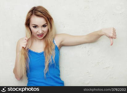 Hair problem. Blond woman holding her damaged dry hair. Teenage girl sticking out tongue and showing thumb down hand sign gesture. Indoor.