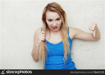 Hair problem. Blond woman holding her damaged dry hair. Teenage girl sticking out tongue and showing thumb down hand sign gesture. Indoor.