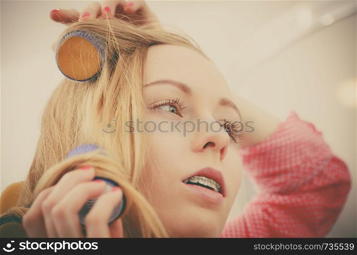 Hair styling at home concept. Woman wearing pajamas curling her hair using rollers in bathroom. Woman curling her hair using rollers