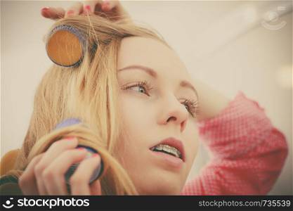 Hair styling at home concept. Woman wearing pajamas curling her hair using rollers in bathroom. Woman curling her hair using rollers