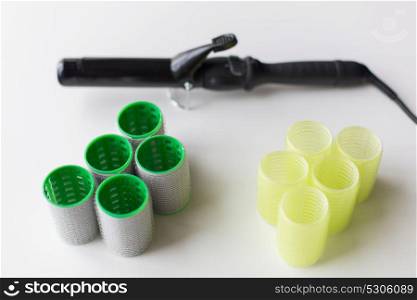 hair tools, beauty and hairdressing concept - curlers or rollers and iron or hot styler on white background. hair curlers or rollers and iron or hot styler
