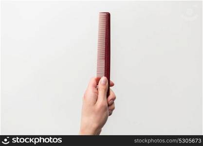 hair tools, beauty and hairdressing concept - hairdresser hand holding brown red comb on white background. hairdresser hand holding brown red hair comb