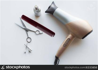 hair tools, beauty and hairdressing concept - hairdryer, scissors, comb and styling spray on white background. hairdryer, scissors, comb and styling hair spray
