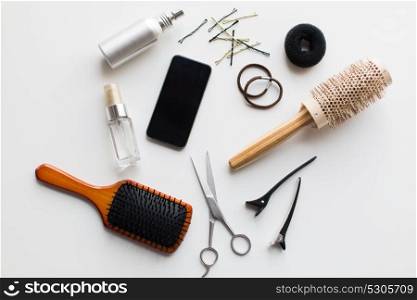 hair tools, beauty and hairdressing concept - smartphone, scissors, brushes and styling sprays with pins and ties on white background. smartphone, scissors, brushes and other hair tools