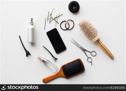 hair tools, beauty and hairdressing concept - smartphone, scissors, brushes and styling sprays with pins and ties on white background. smartphone, scissors, brushes and other hair tools