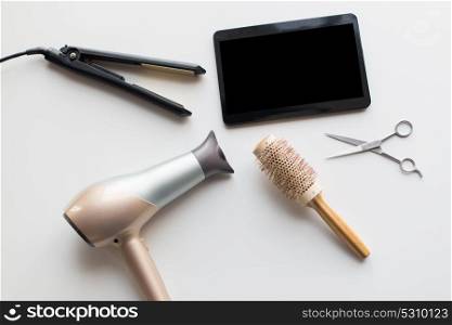 hair tools, beauty and hairdressing concept - tablet pc, scissors, hairdryer with hot styling iron and curling brush on white background. tablet pc, scissors, hairdryer, hot iron and brush
