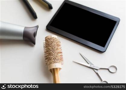 hair tools, beauty and hairdressing concept - tablet pc, scissors, hairdryer with hot styling iron and curling brush on white background. tablet pc, scissors, hairdryer, hot iron and brush