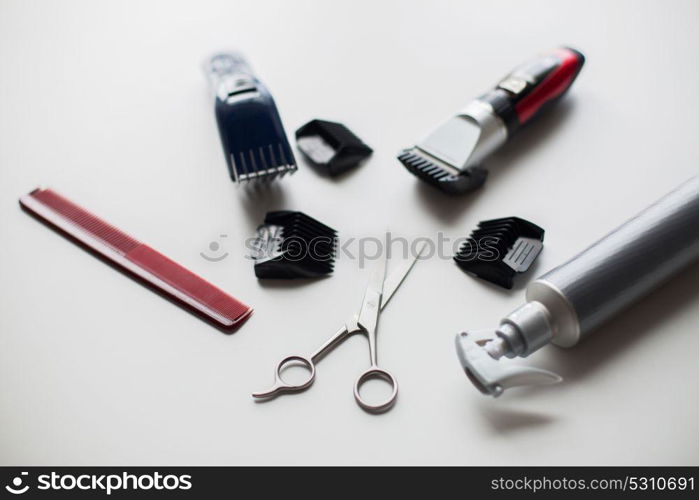 hair tools, hairstyle and hairdressing concept - styling sprays, trimmers or clippers with scissors and attachment combs on white background. styling hair sprays, clippers, comb and scissors