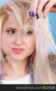 Haircare and hairstyling, bad effects of bleaching concept. Blonde woman holding her damaged, split hair ends looking sad and angry.. Blonde woman holding her hair ends