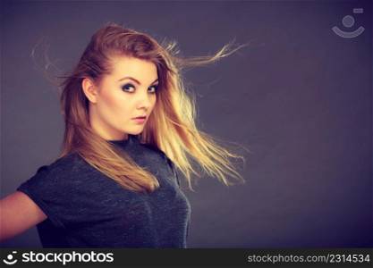 Haircare, beauty, hairstyling concept. Portrait of young attractive blonde woman wearing dark t shirt having windblown beautiful long hair.. Attractive blonde woman with windblown hair