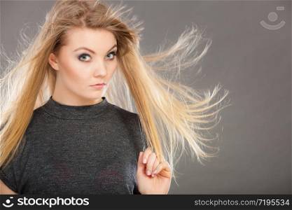 Haircare, beauty, hairstyling concept. Portrait of young attractive blonde woman wearing dark t shirt having windblown beautiful long hair.. Attractive blonde woman with windblown hair
