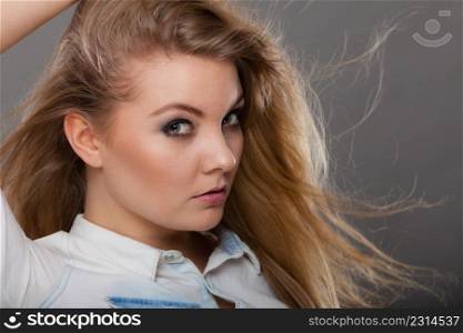 Haircare, beauty, hairstyling concept. Portrait of young attractive blonde woman wearing white shirt having windblown beautiful long hair.. Attractive blonde woman with windblown hair