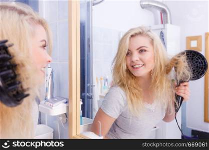 Haircare. Beauty long haired blonde woman drying hair in bathroom. Smiling girl blowing wind on wet head using hairdryer, doing curls with diffuser nozzle.. Woman doing curls with hairdryer diffuser