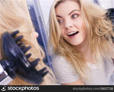 Haircare. Beauty long haired blonde woman drying hair in bathroom. Smiling girl blowing wind on wet head using hairdryer, doing curls with diffuser nozzle.. Woman doing curls with hairdryer diffuser