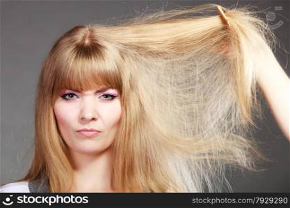 Haircare. Blonde woman with her damaged dry hair angry face expression gray background