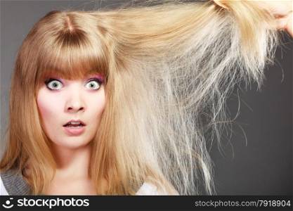 Haircare. Blonde woman with her damaged dry hair shocked face expression gray background