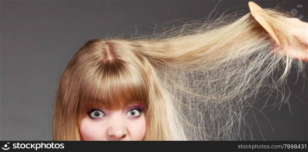 Haircare. Blonde woman with her damaged dry hair wide eyed gray background