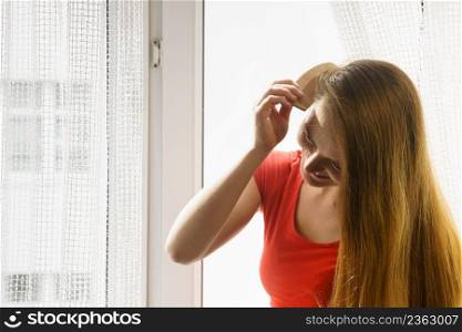 Haircare, morning routine concept. Woman sitting on windowsill brushing her long dark hair with comb.. Woman sitting on windowsill brushing her hair