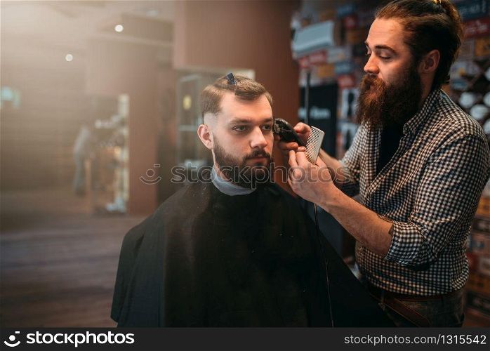 Haircutter makes hairstyle of the client man in black salon cape by clipper. Barbershop concept