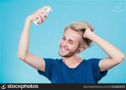 Hairdo haircare and makes hairstyle concept. Handsome young guy, fashion blonde metrosexual model applying spray cosmetic to his hair. Man applying spray cosmetic to his hair
