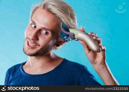 Hairdo hairstyle concept. Cool male hairstylist making self trendy haircut, fashion blonde metrosexual model going to shave his long hair. Man going to shave his long hair