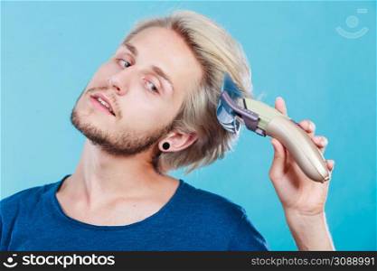 Hairdo hairstyle concept. Cool male hairstylist making self trendy haircut, fashion blonde metrosexual model going to shave his long hair. Man going to shave his long hair