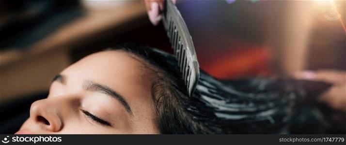 Hairdresser applying revitalizing pack on woman’s long black hair.. Hairdresser Treating Woman’s Hair with Revitalizing Hair Pack