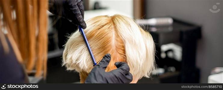 Hairdresser combing female short blonde hair before dyeing in a hair salon. Hairdresser combing female short hair