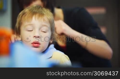 Hairdresser combing hair of the little boy before haircut. Focus on the lovely calm boy