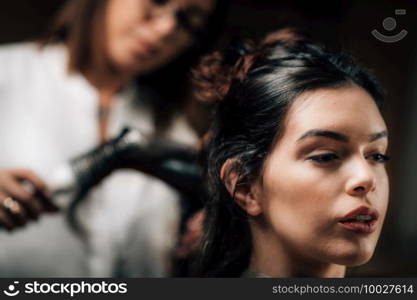 Hairdresser curling woman’s long black hair with brush and hair dryer.. Hairdresser Curling Woman’s Hair